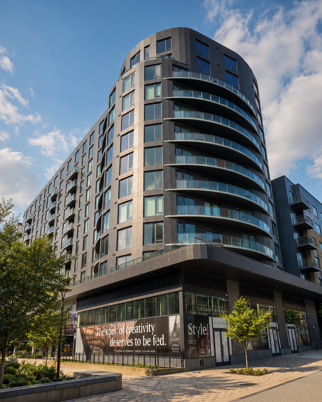 Modern curved apartment building with dark gray facade, glass balconies, and ground-floor retail.