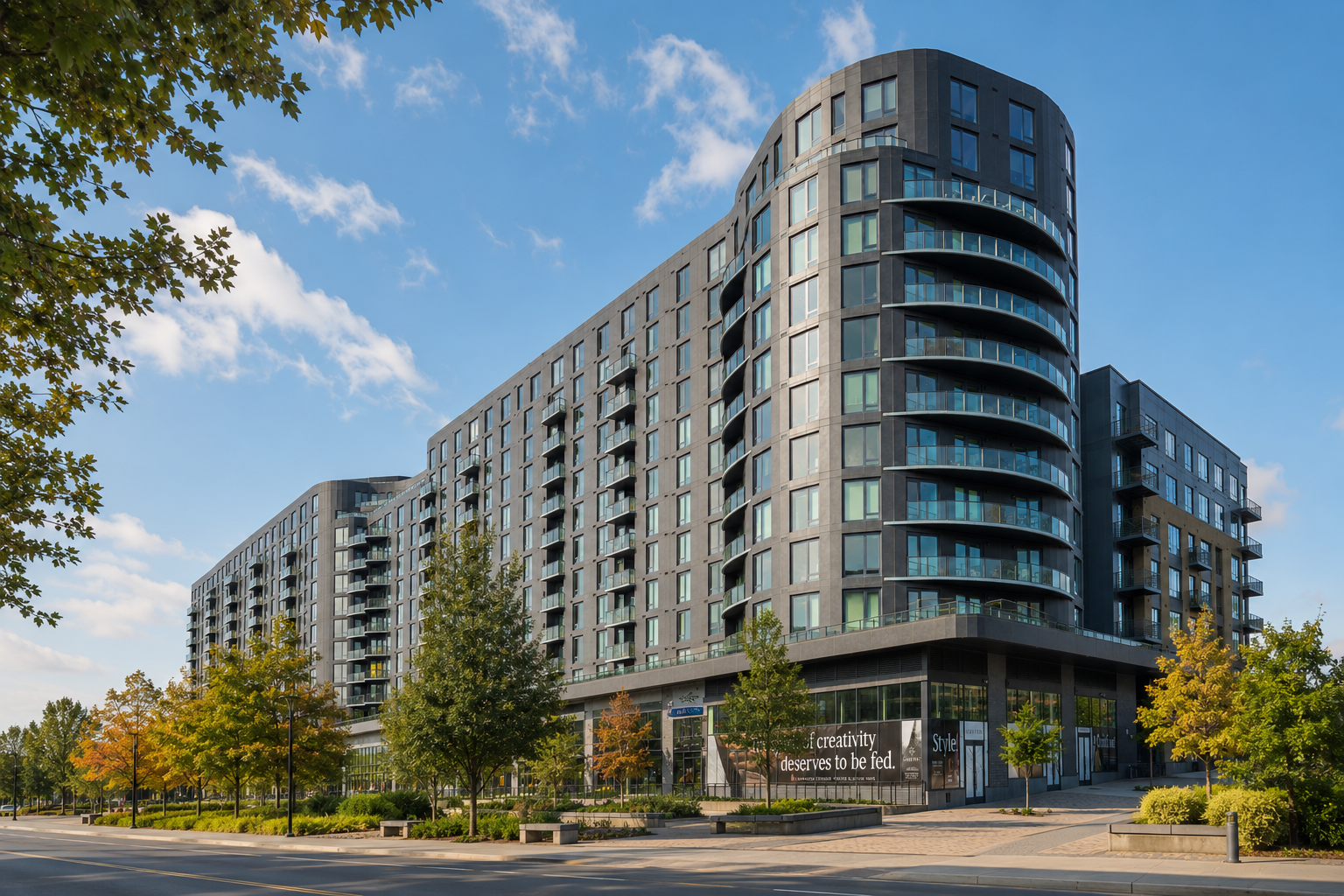Wide street view of a large contemporary apartment complex with landscaped sidewalks and trees.