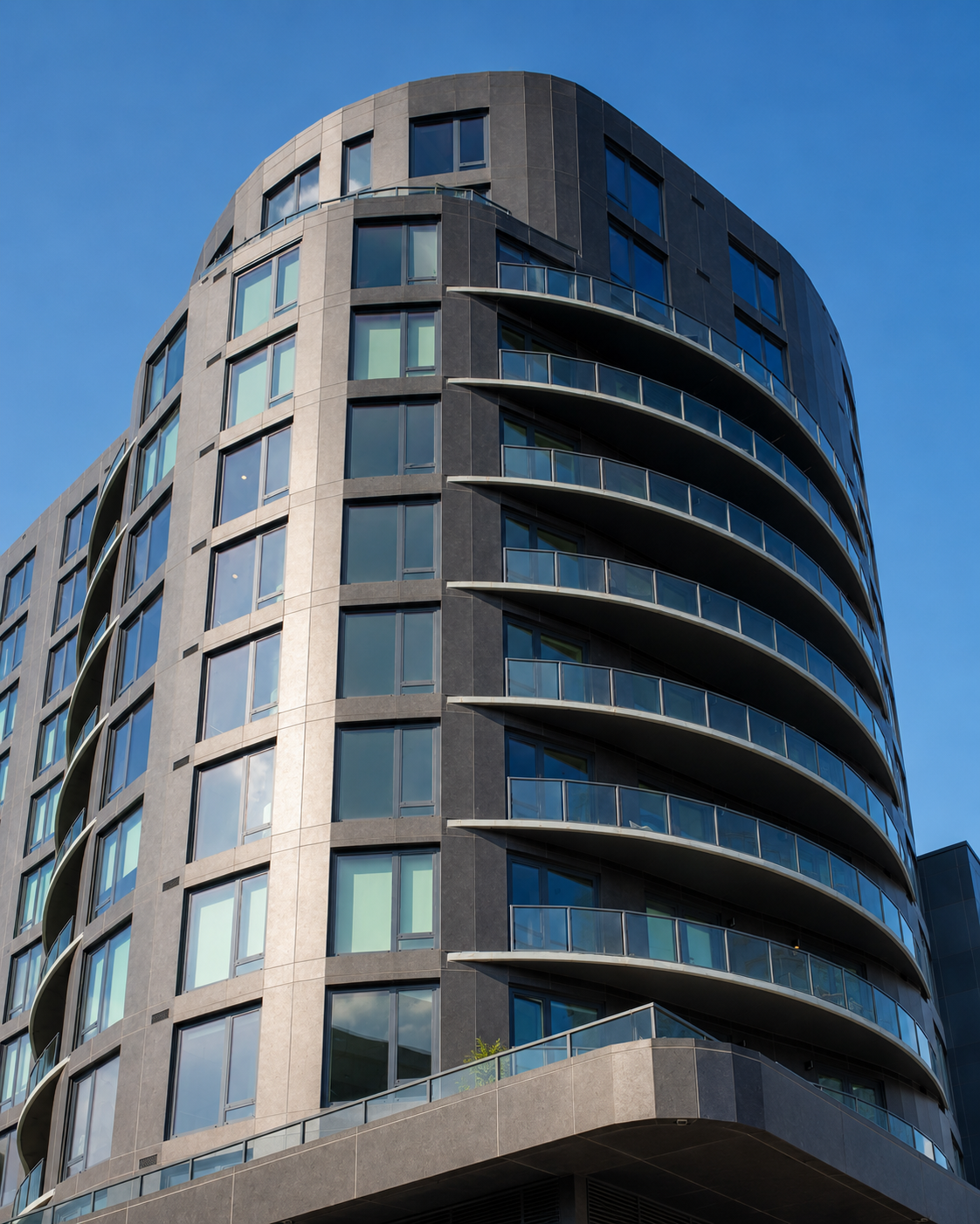 Close-up of a rounded dark gray residential tower with stacked glass balconies.